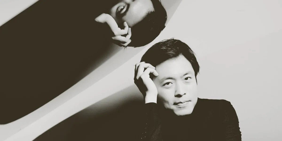 Sunwook Kim rests his head on his hands, reflected in an open piano